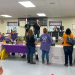 A couple people purchasing basket raffle ticket sheets during an intermission at the Breaking the Silence Mystery Bingo.